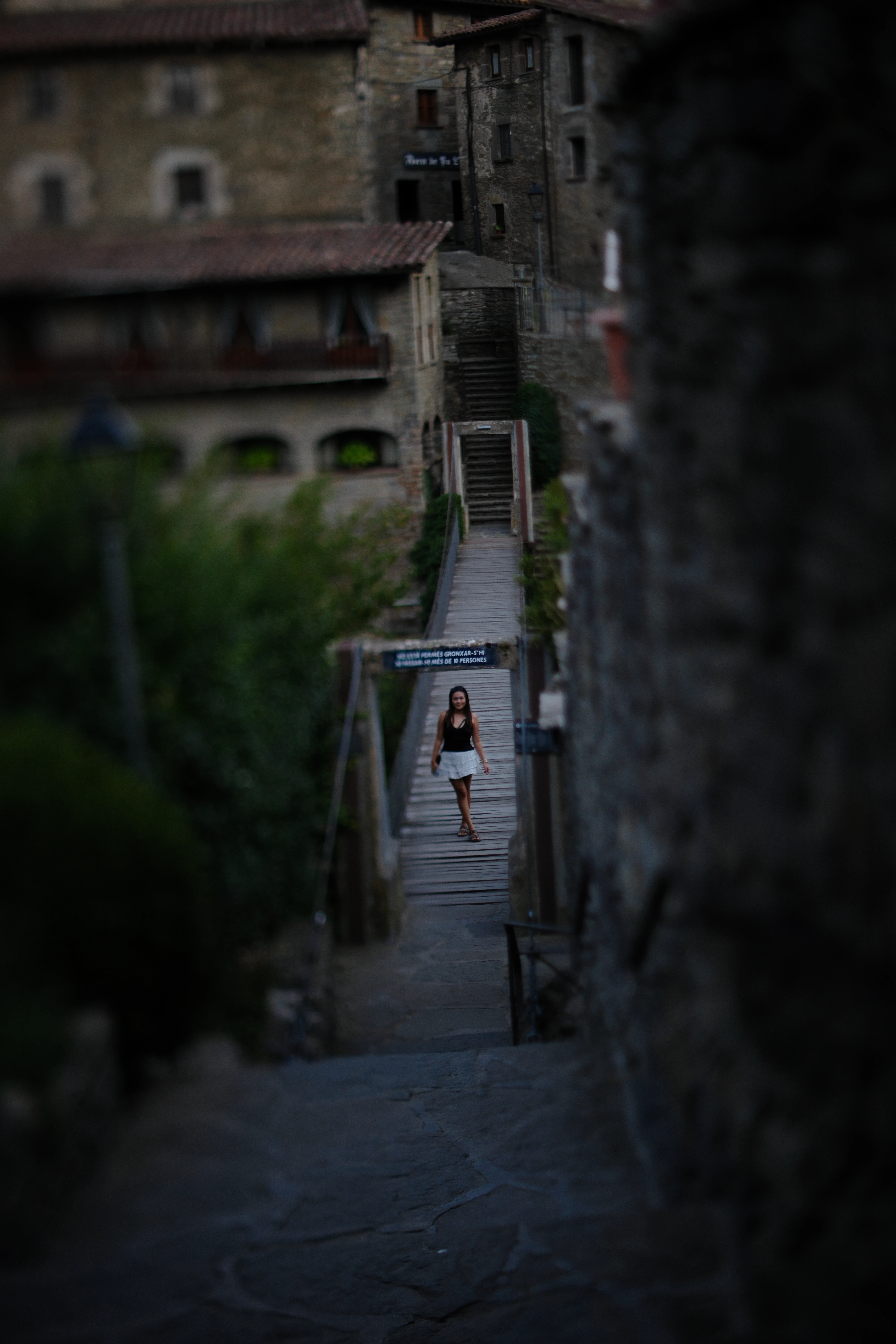 A woman crossing a narrow footbridge between stone buildings, isolated by selective focus