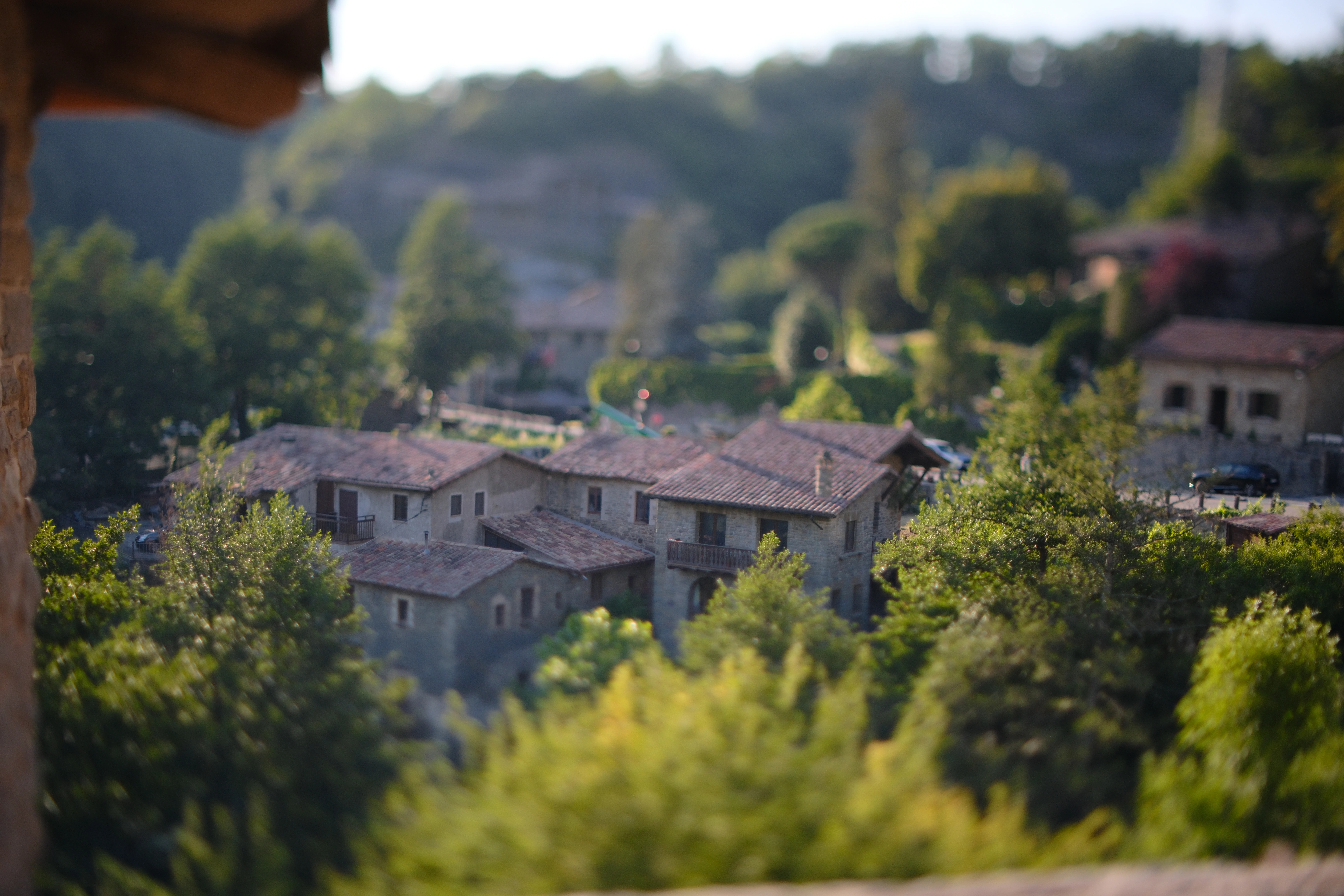 Stone houses in Rupit seen across trees and a sunlit foreground through tilt focus