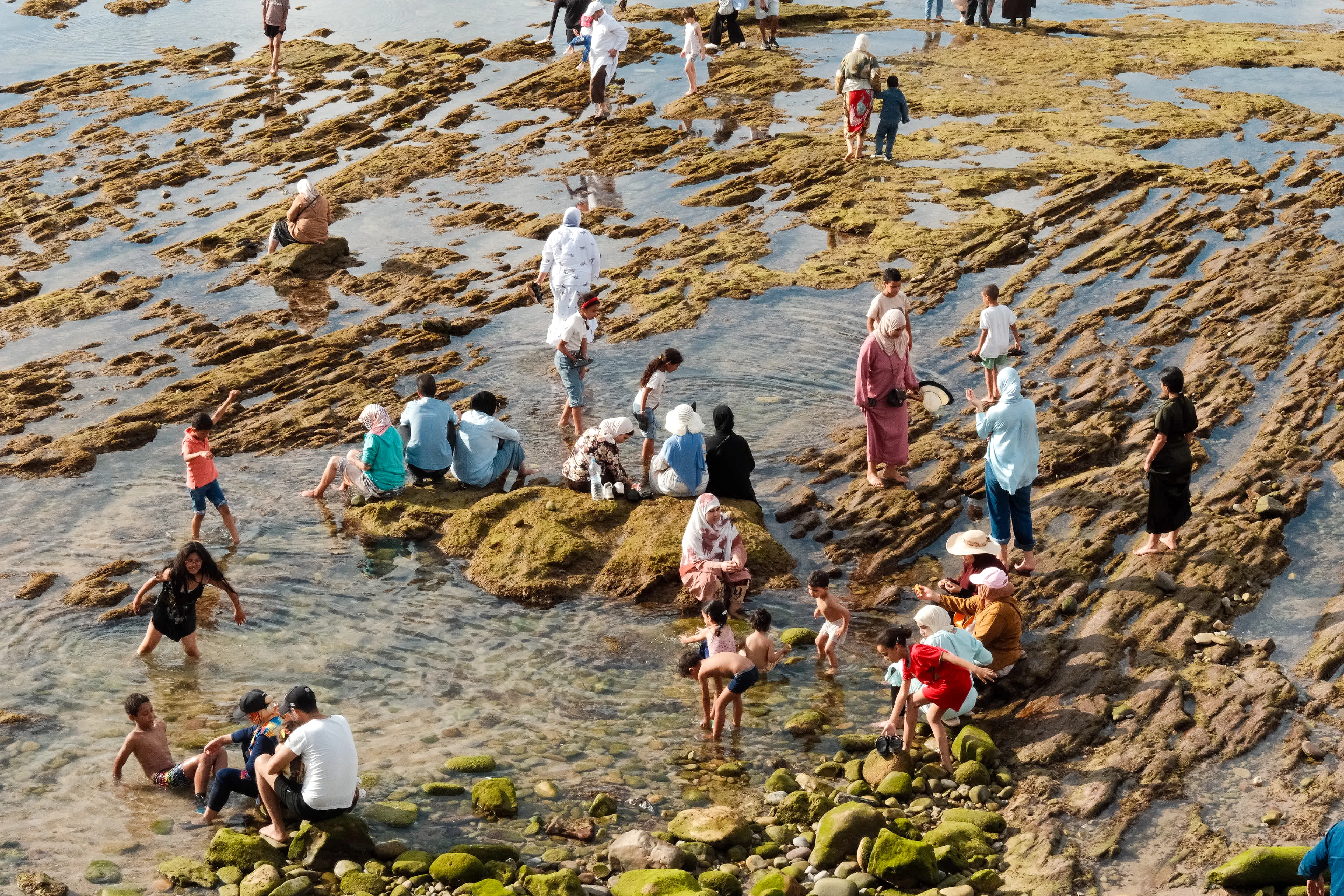 Families and children gather among shallow tidal pools on the rocky coast