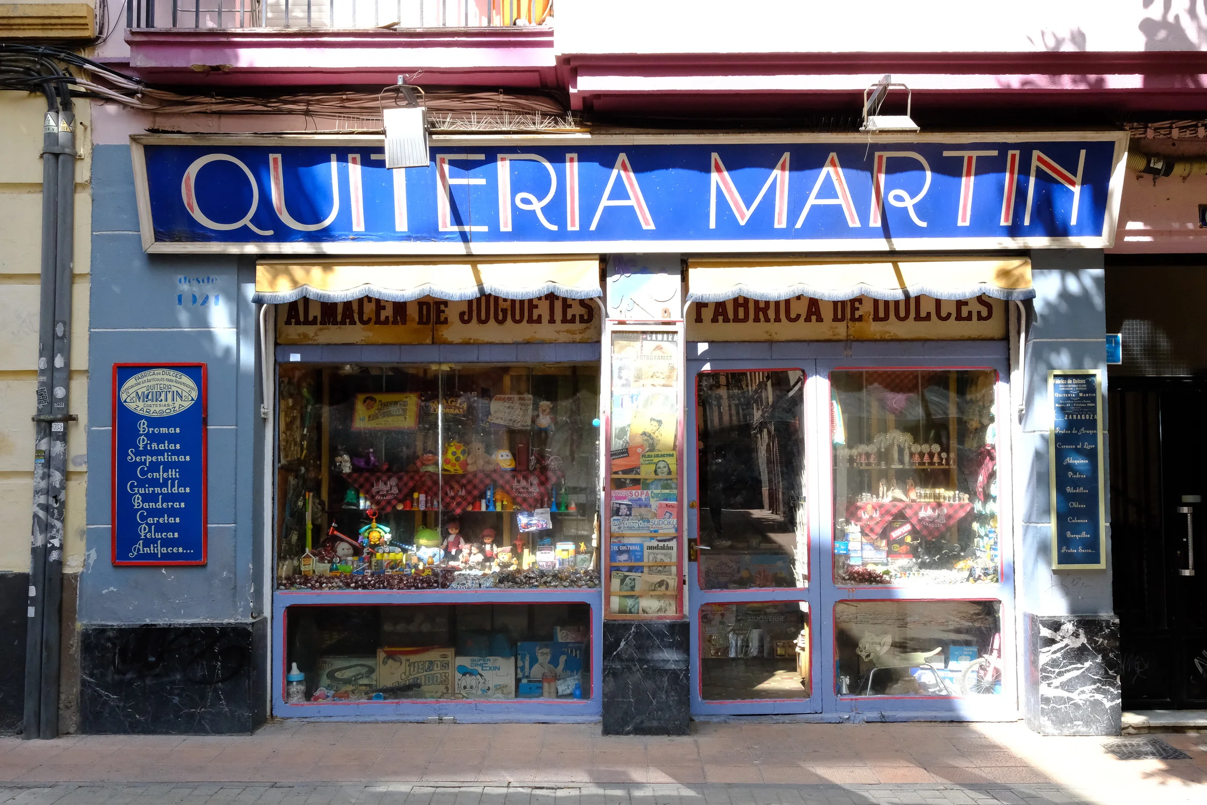 A blue and red vintage sweet shop facade filled with toys and window reflections