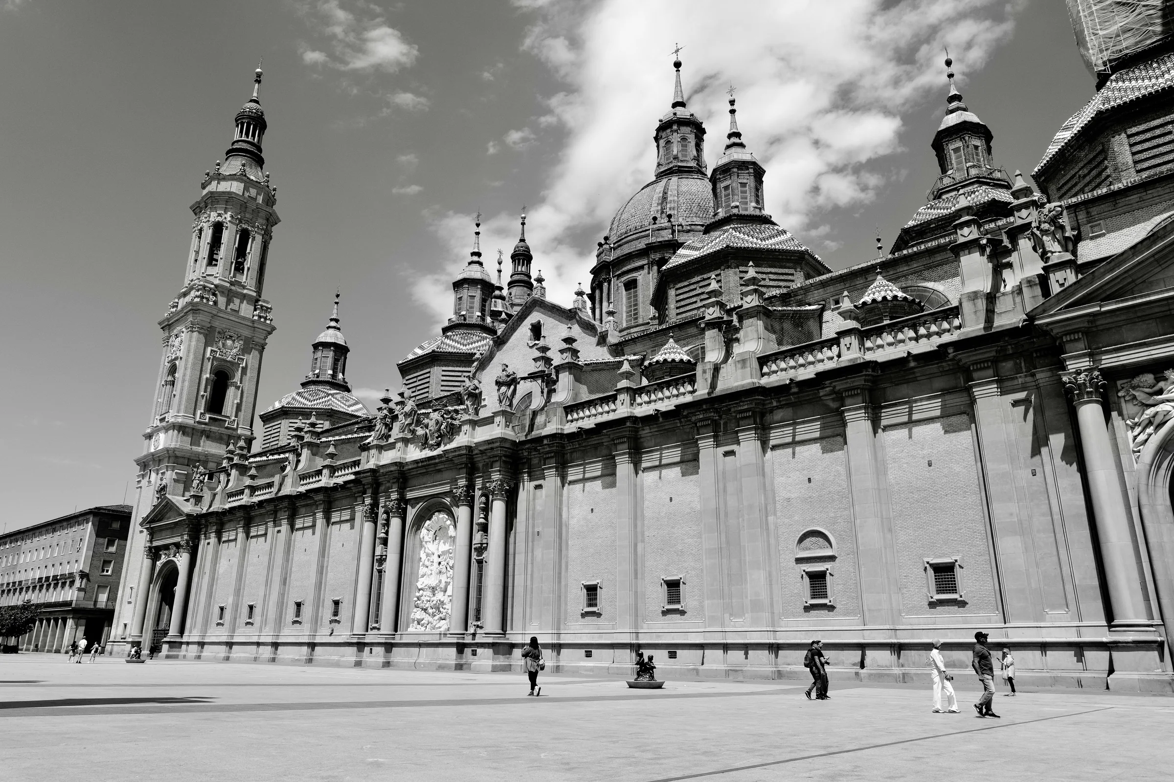 The Basilica del Pilar facade in black and white with small figures crossing the plaza