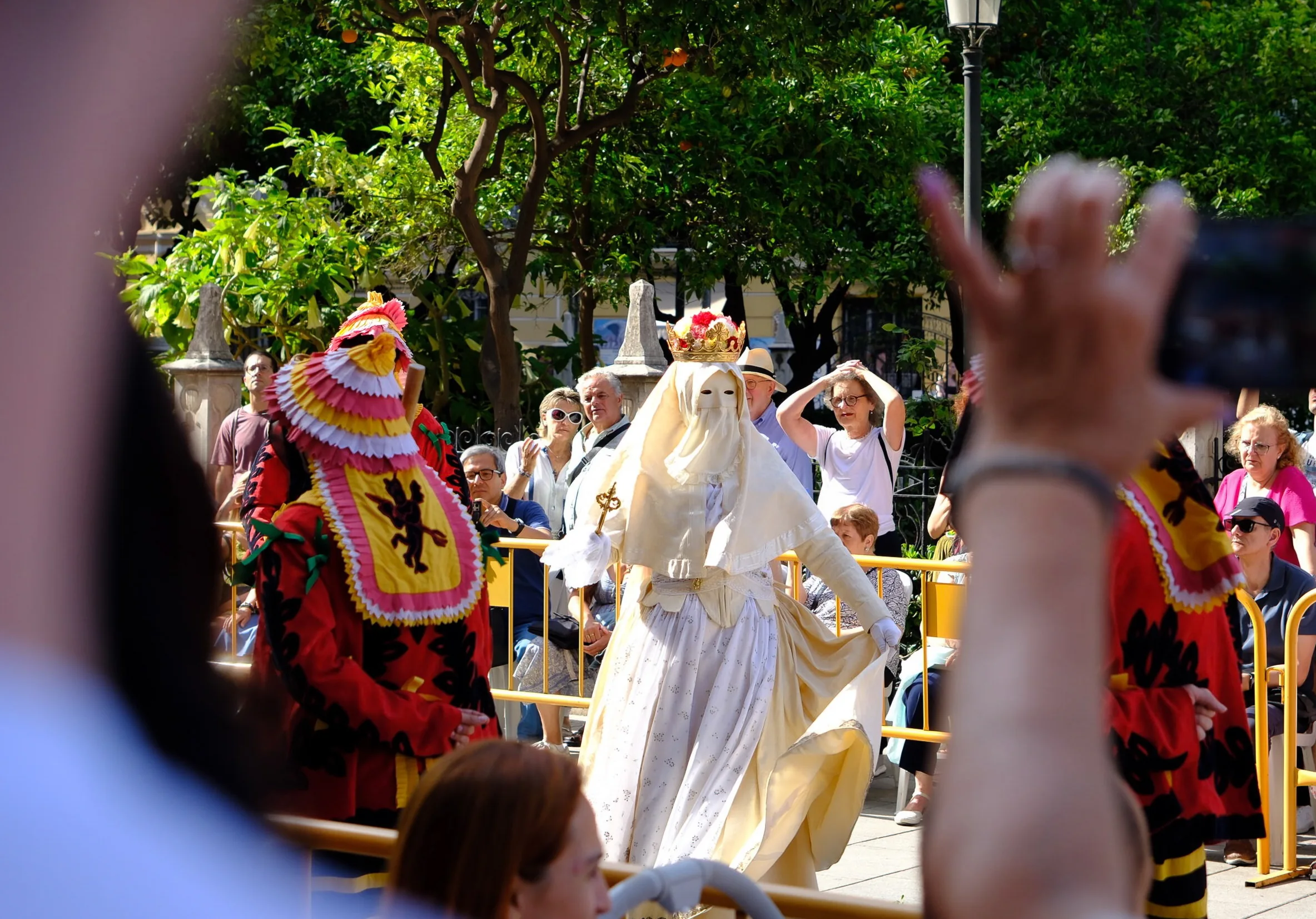 Festival figures pass through a crowd while a raised hand records on a phone