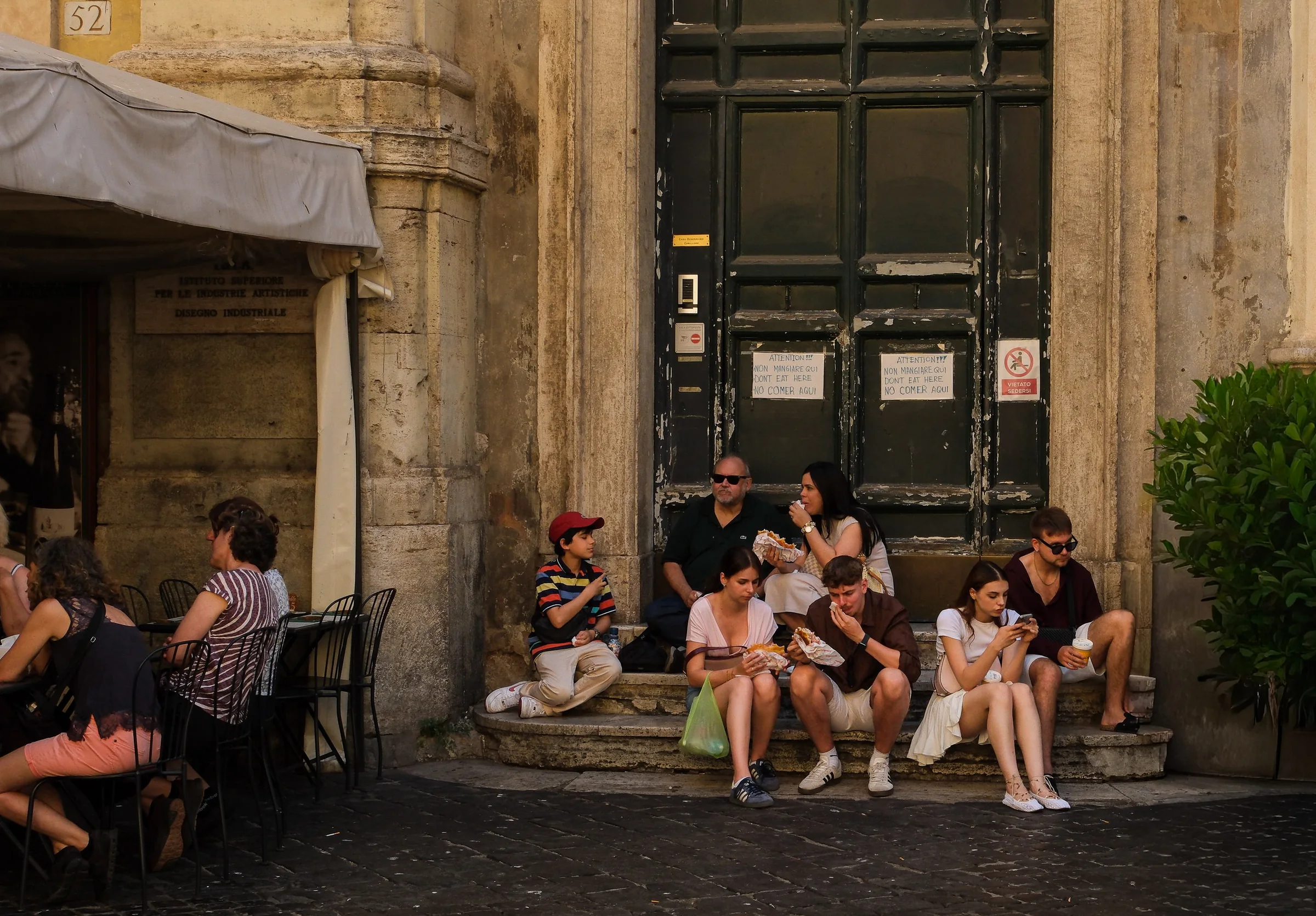 People sit eating on stone steps below signs asking visitors not to eat there