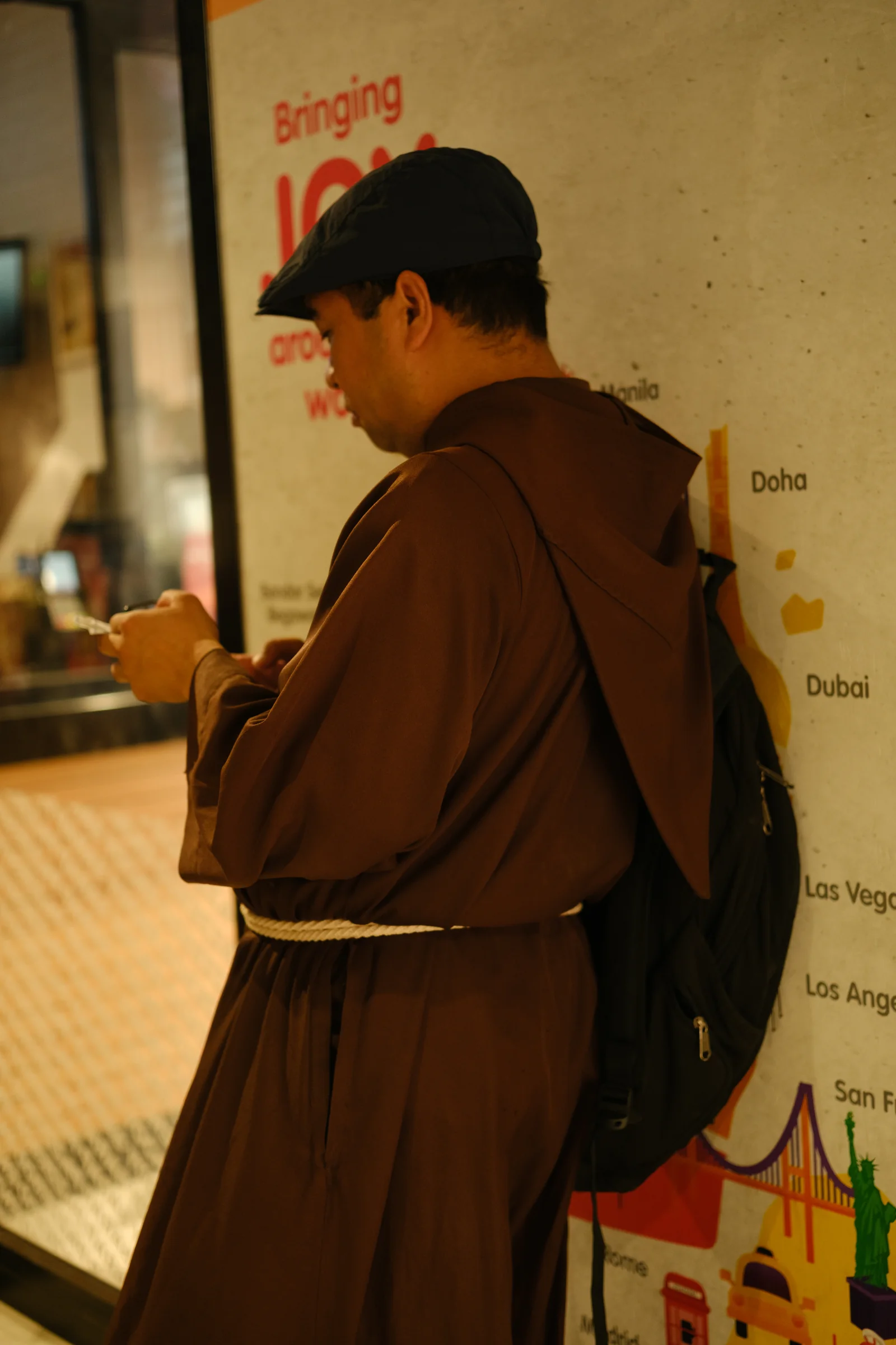 A person in a brown robe stands beside a transit map and warm station light