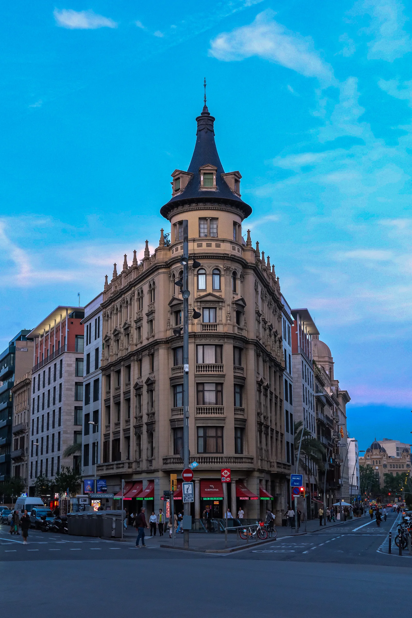 A vertical Barcelona corner building rises into a bright blue evening sky